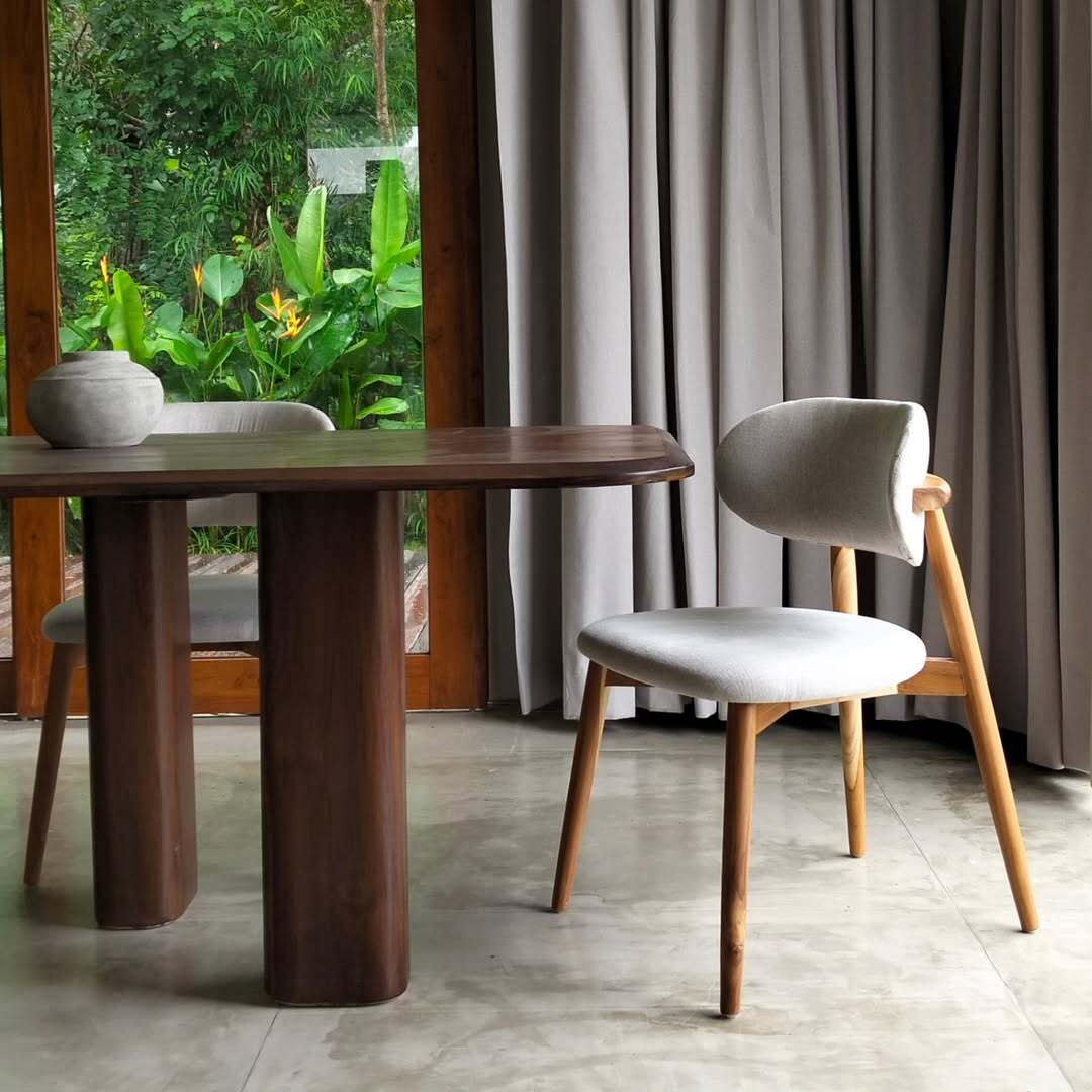 Intérieur salle à manger moderne avec table en bois foncé et chaises en tissu clair, ouvrant sur une végétation luxuriante.