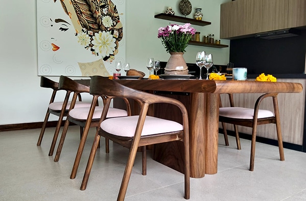 Salle à manger moderne avec table en bois massif, chaises courbées à coussins roses, et une grande peinture murale d'un visage féminin fleuri.