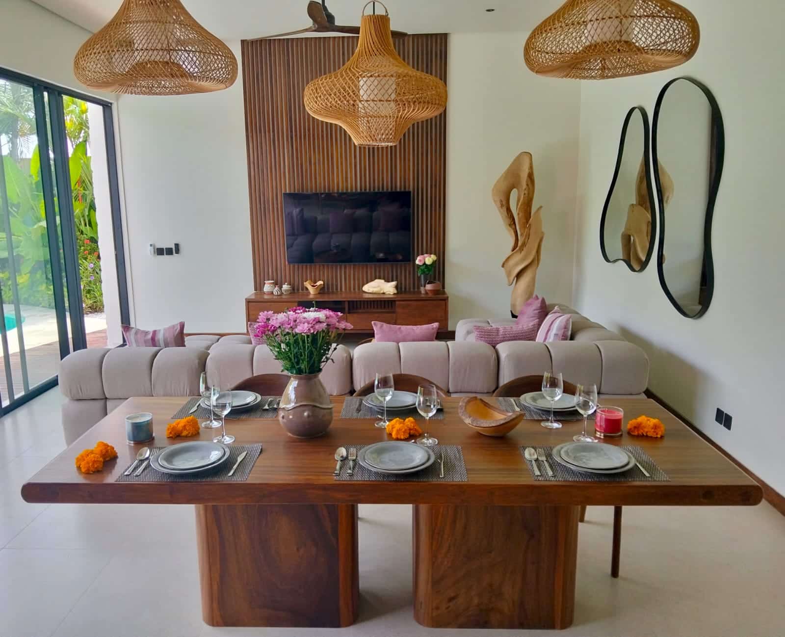 Salle à manger moderne et lumineuse avec table en bois massif, suspensions en rotin et canapé incurvé, ambiance tropicale chic.