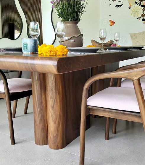 Table à manger en bois foncé aux pieds arrondis, décorée de fleurs jaunes, bougies et verres à vin.