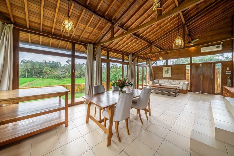 Spacieuse salle à manger/salon tropicale avec plafond en bois, ouvrant sur une vue luxuriante de rizière et décorée avec élégance.