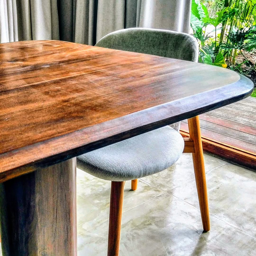 Table à manger bois massif aux bords arrondis, avec une chaise moderne gris clair et vue sur verdure extérieure.